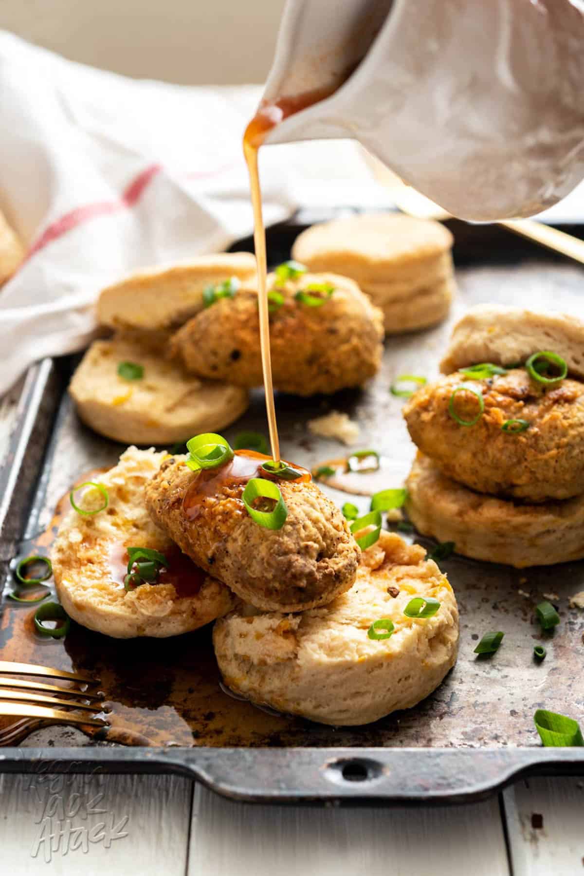 drizzling syrup on vegan chicken and biscuits spread on a baking sheet.