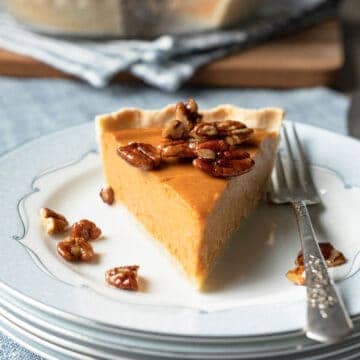 A slice of pie on a plate topped with candied pecans.