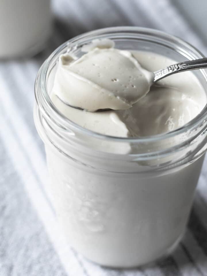 thick and creamy vegan yogurt on a spoon resting over a jar.