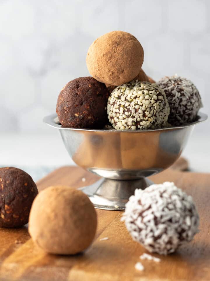 raw vegan energy balls with different coatings stacked in a silver bowl.