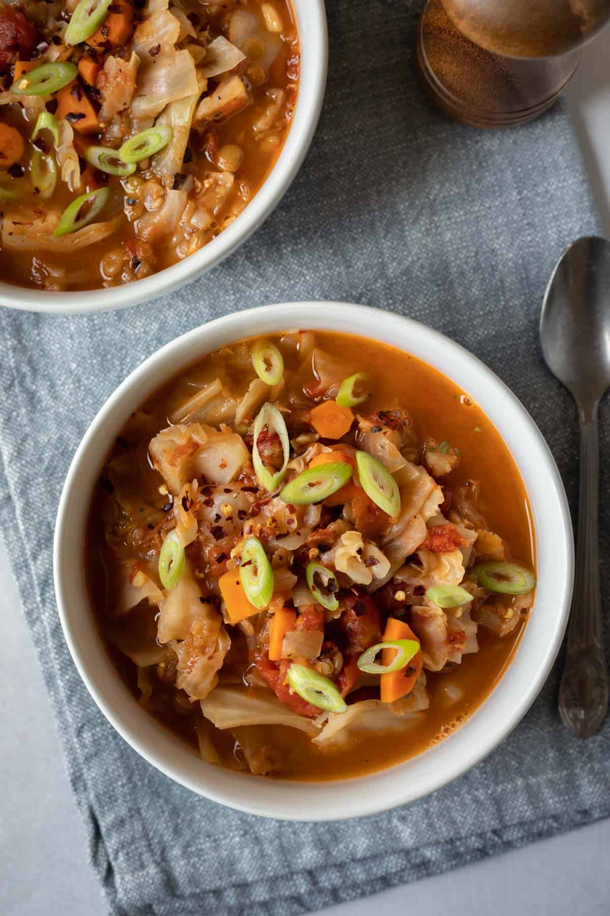 overhead view of cabbage soup in white bowls against a blue background.