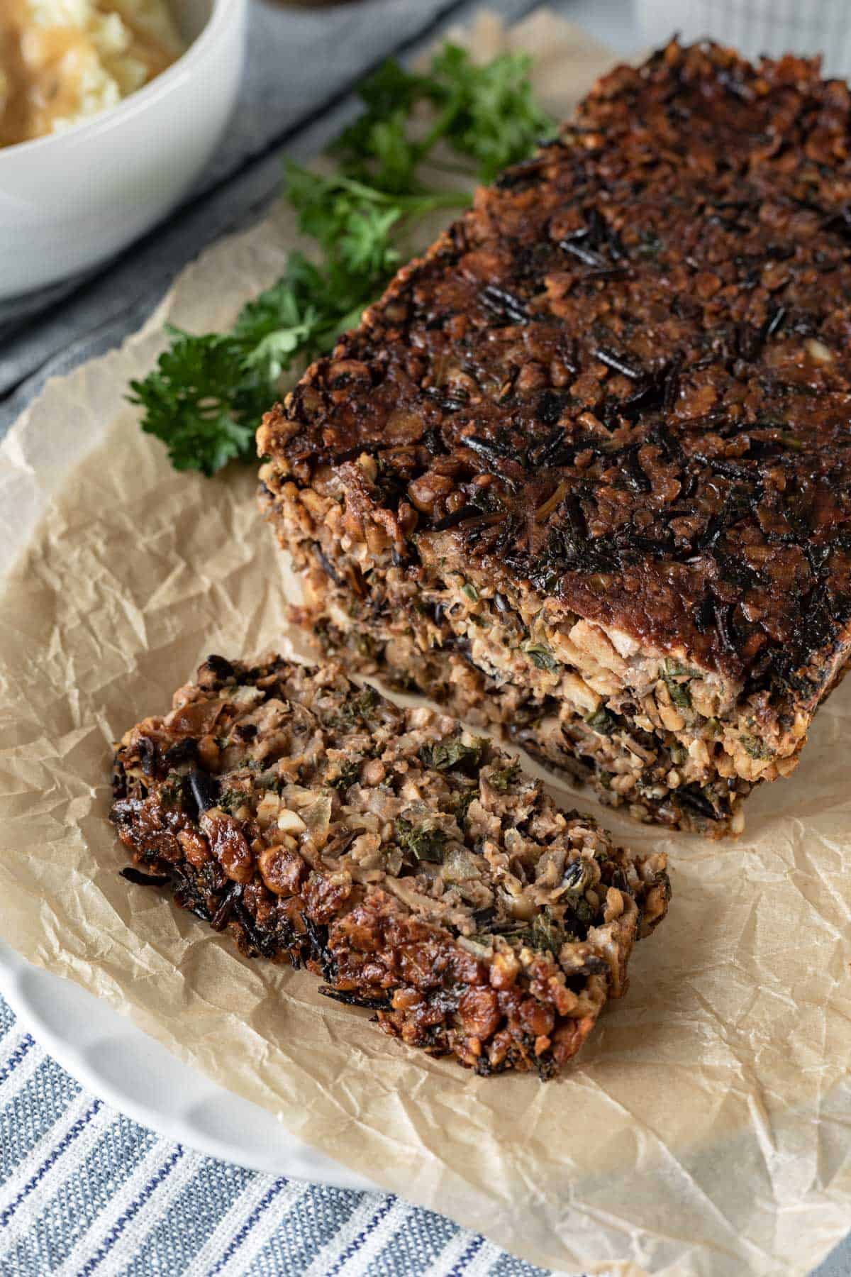 chunky vegan meatloaf filled with chickpeas, wild rice, and veggies on a white platter.