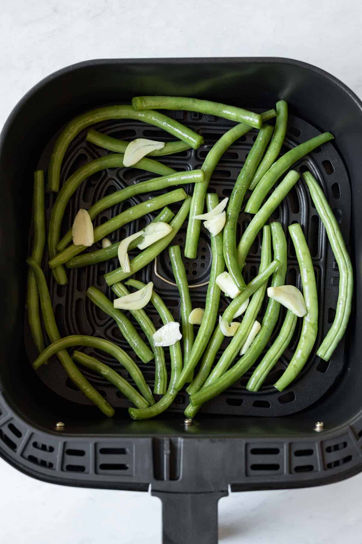 green beans and sliced garlic in single layer inside air fryer basket.