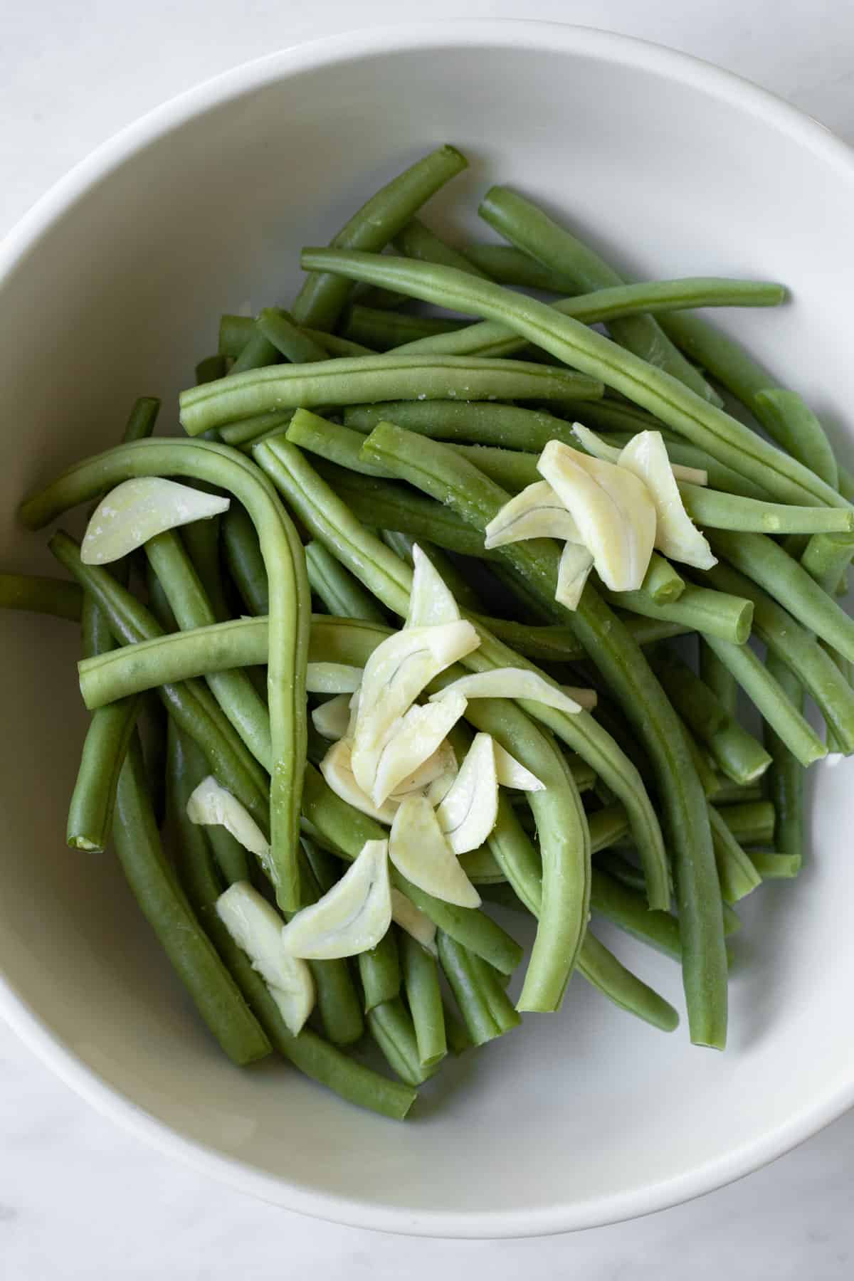tossing green beans with garlic and oil in a large bowl.