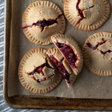 overhead view of hand pies on a baking sheet with red cranberry filling peeking through.