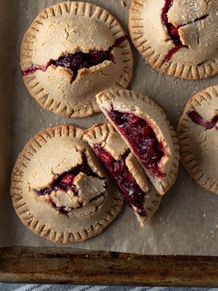 overhead view of hand pies on a baking sheet with red cranberry filling peeking through.