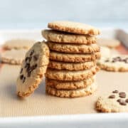 close up of crisp cookies stacked on baking sheet, some with chocolate chips.