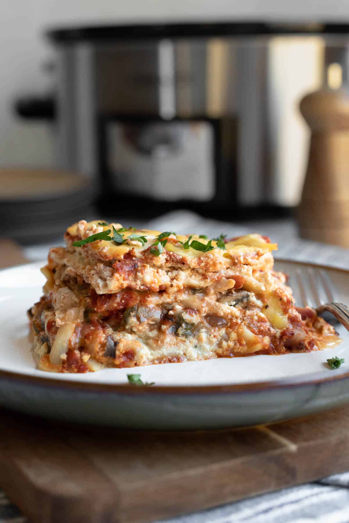 a serving of vegan lasagna on a white plate with crockpot in background.