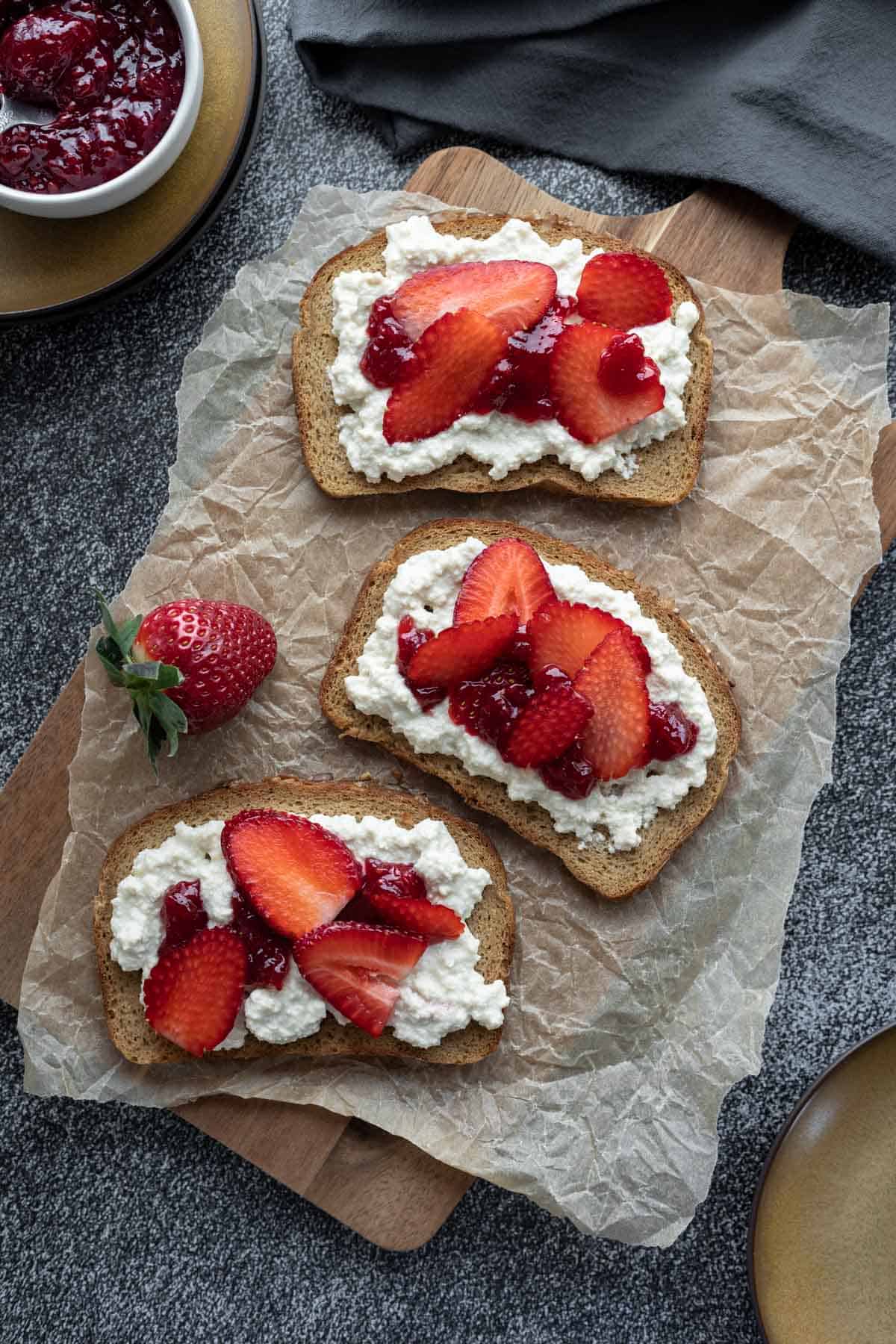 3 slices of bread topped with vegan cottage cheese, jam, and sliced strawberries.