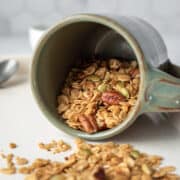a mug tipped on its side with crunchy granola spilling out.