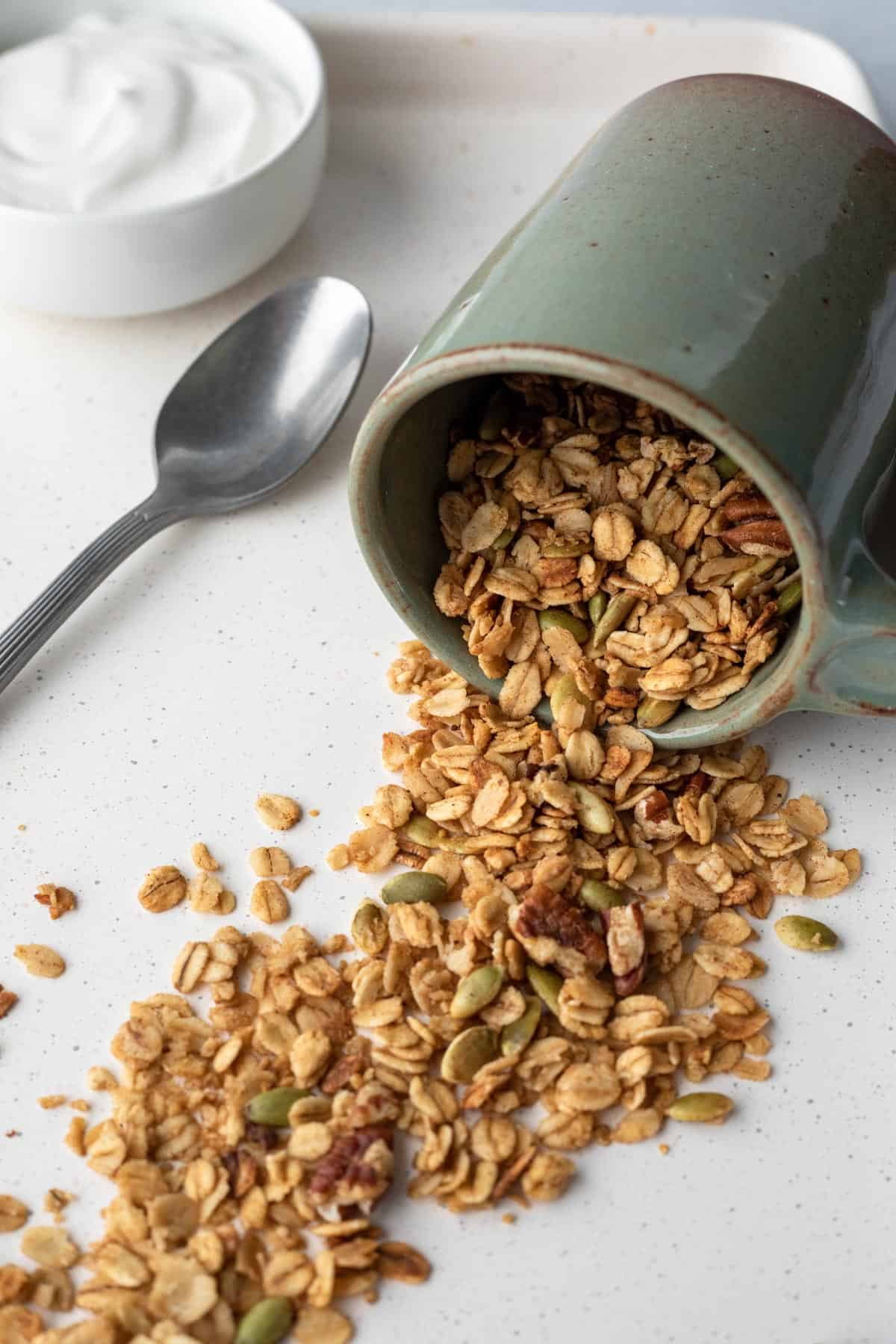 a green mug on its side with crunchy vegan microwave granola spilling out.