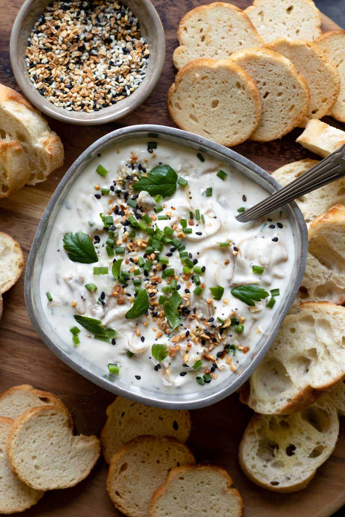 caramelized vegan onion dip in a serving bowl topped with parsley and surrounded by bread.