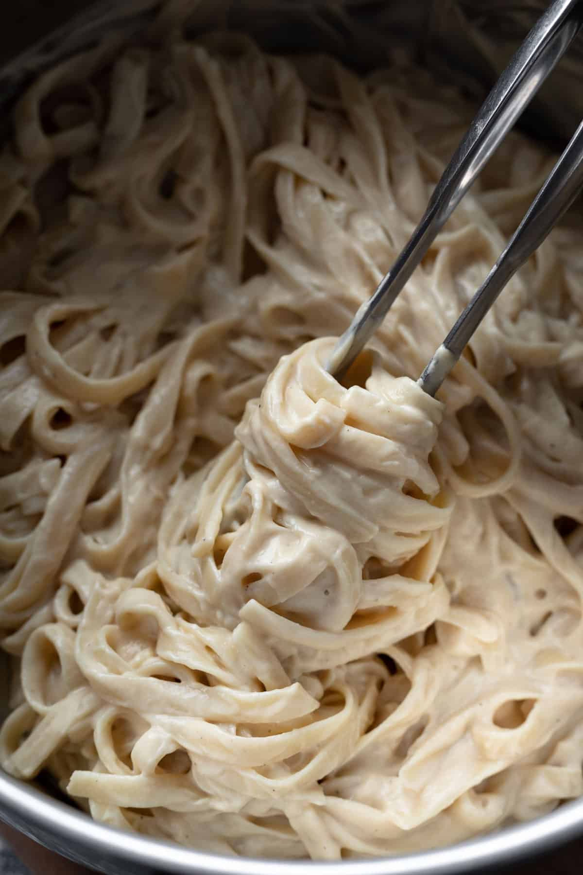 twirling creamy fettuccine alfredo with tongs inside a pasta pot.