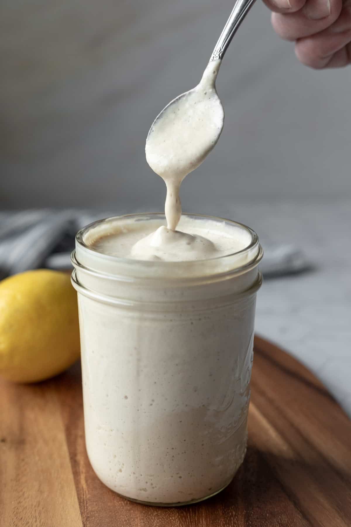 creamy sunflower seed dressing dripping from a spoon into a glass jar.