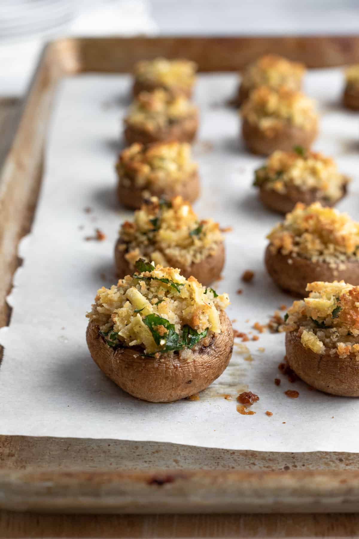 golden breadcrumb topped vegan stuffed mushrooms lined up on a baking sheet.