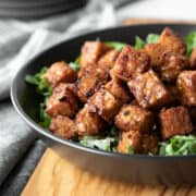 side view of crispy and sticky tempeh in a black bowl.