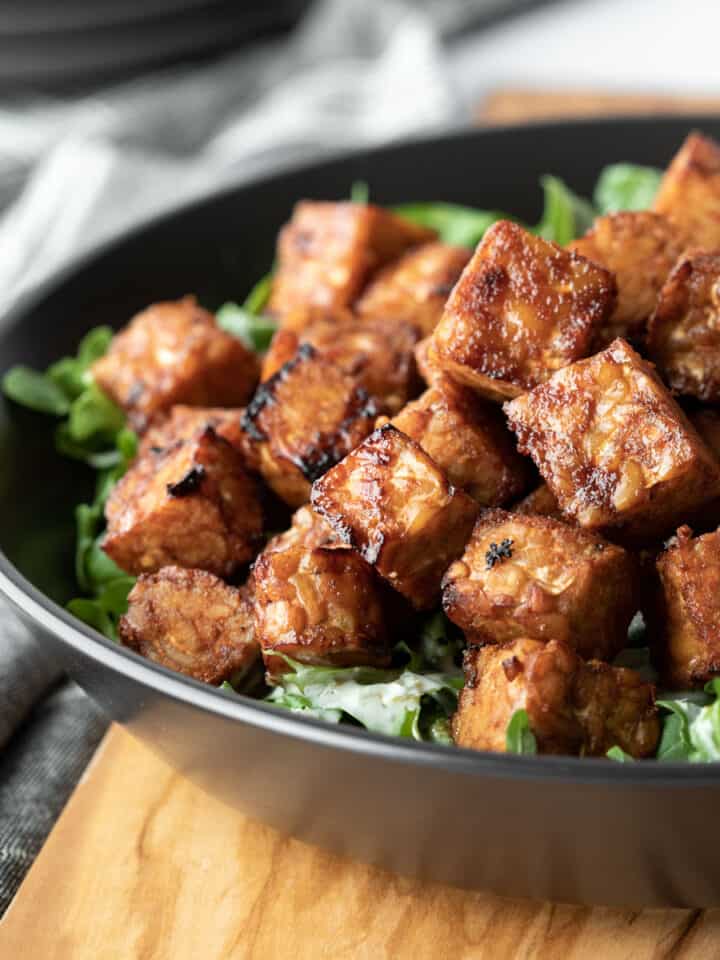 side view of crispy and sticky tempeh in a black bowl.
