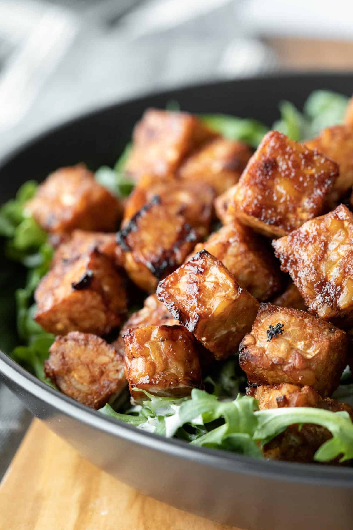 close up of sweet and sticky cubes of air fried tempeh on top of greens.