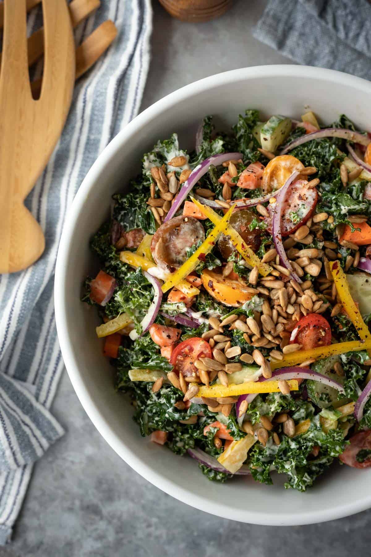 A white serving bowl filled with colorful vegan kale salad.
