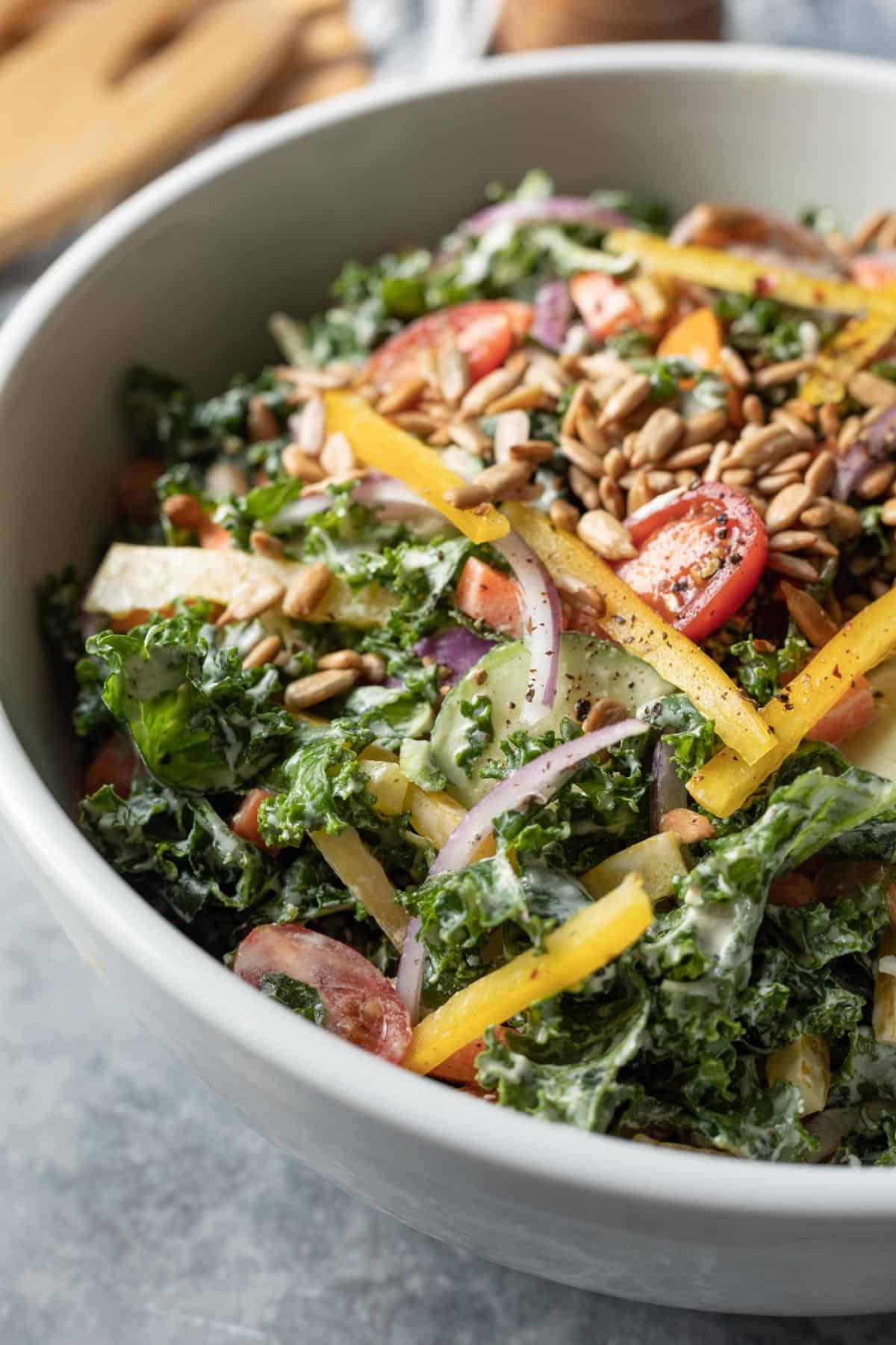 side view of nut-free kale salad in a white serving bowl topped with sunflower seeds.