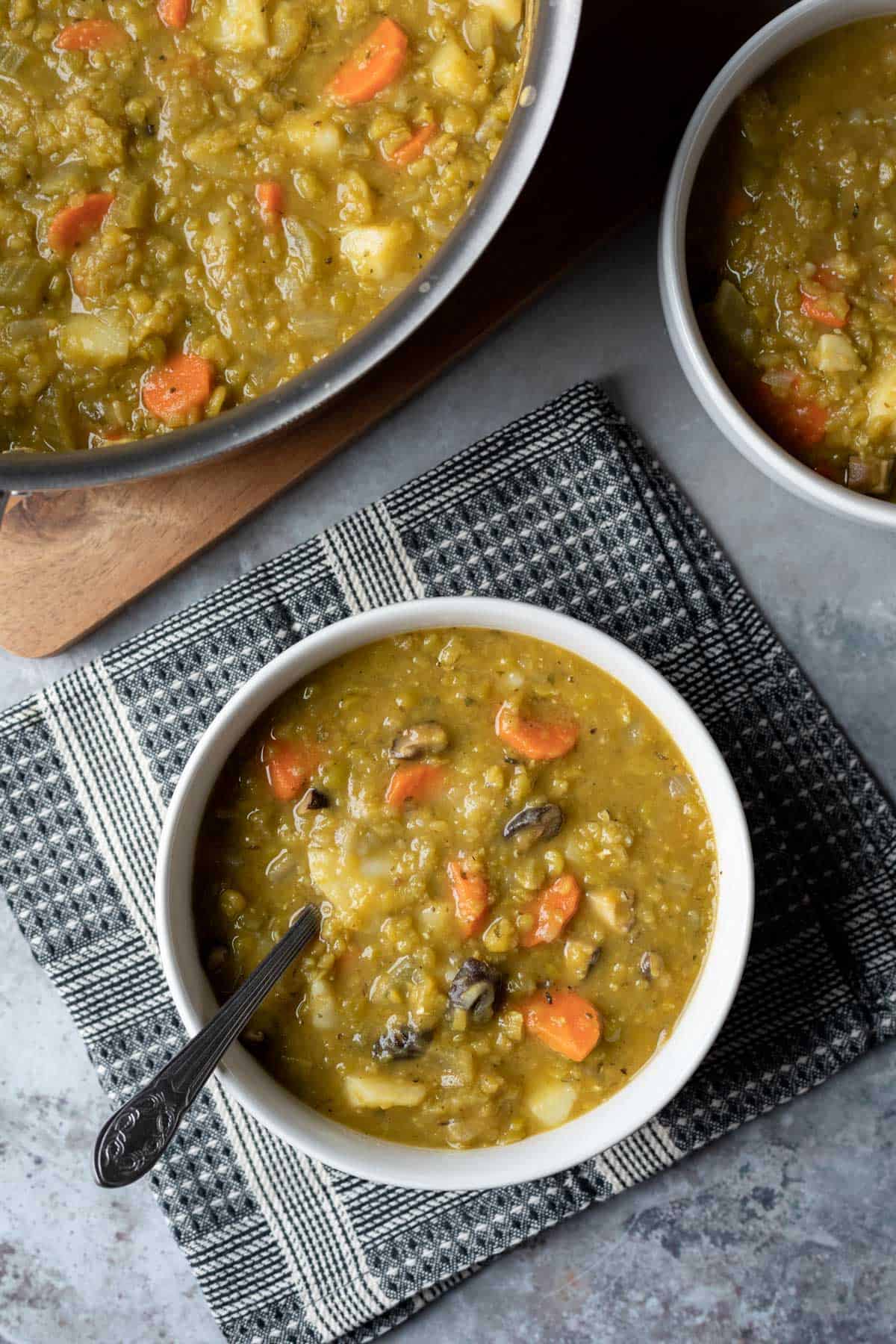 servings of pea soup in white bowls with soup pot in background.