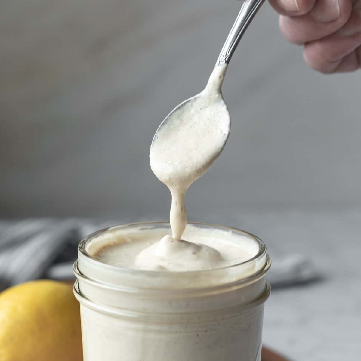 hand holding a spoon that's dripping creamy vegan dressing into a jar.