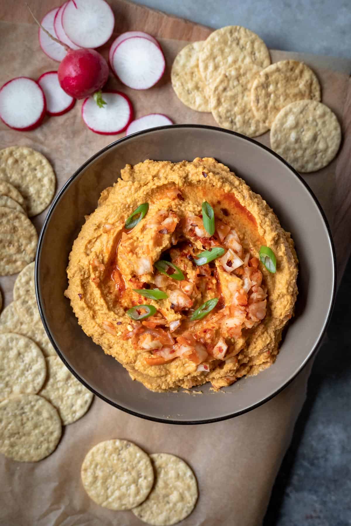 overhead view of colorful orange hummus in a bowl surrounded by crackers.