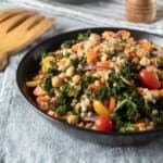 kale salad with couscous, chickpeas, and vegetables in a black bowl.