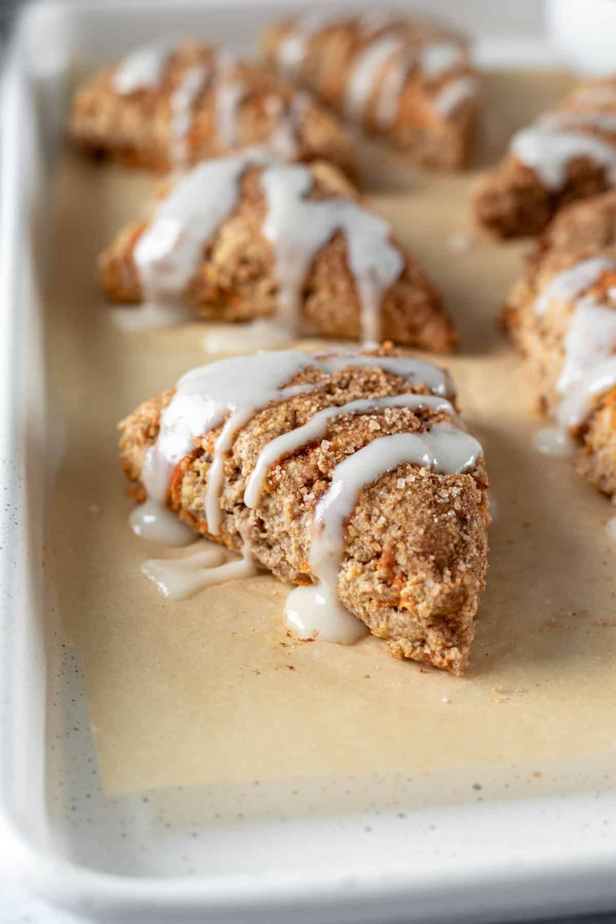 carrot cake scones drizzled with coconut butter icing on a parchment lined baking sheet.