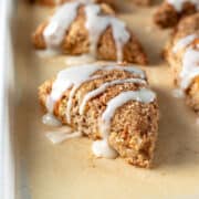 vegan scones drizzled with coconut butter icing on a parchment lined baking sheet.