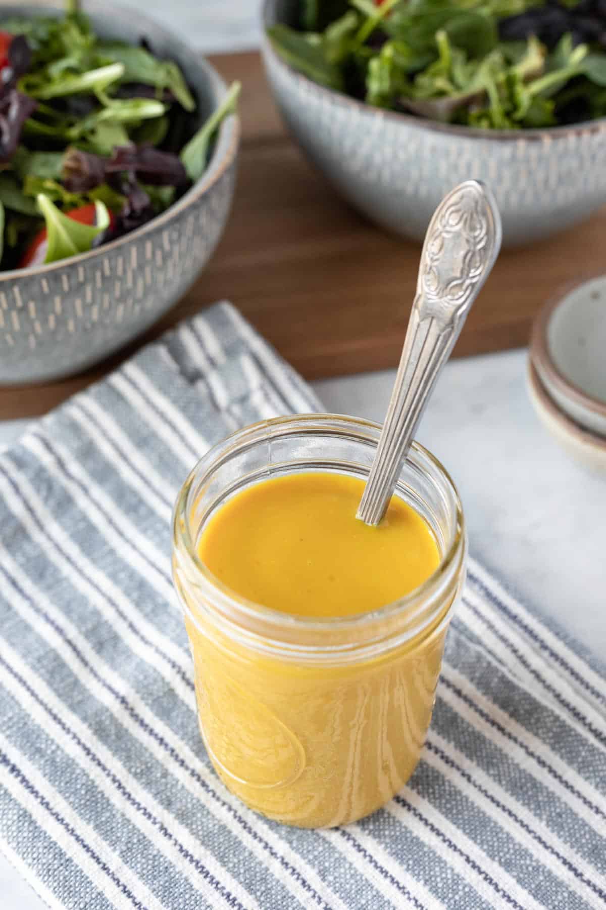 vegan honey mustard dressing in a glass jar with bowls of salad in background.