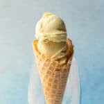 scoops of vegan lemon ice cream in a waffle cone against a blue background.