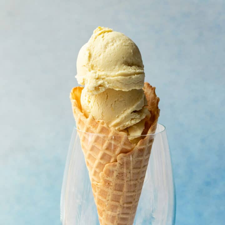 scoops of vegan lemon ice cream in a waffle cone against a blue background.