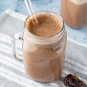 close up of chocolatey hemp milk in a glass jar with a glass straw.