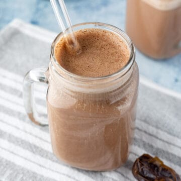 close up of chocolatey hemp milk in a glass jar with a glass straw.