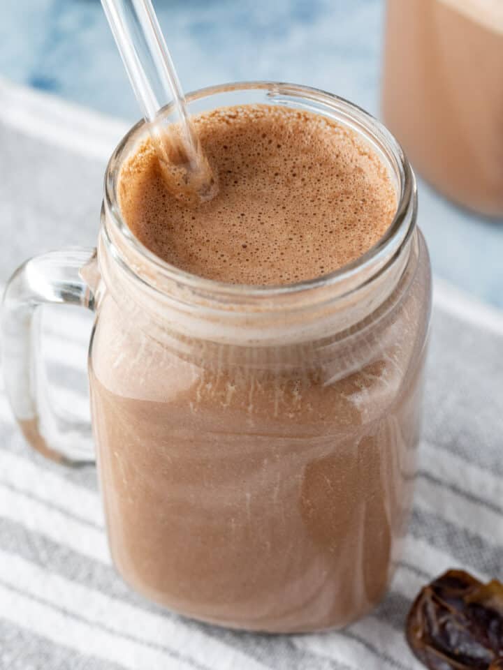 close up of chocolatey hemp milk in a glass jar with a glass straw.