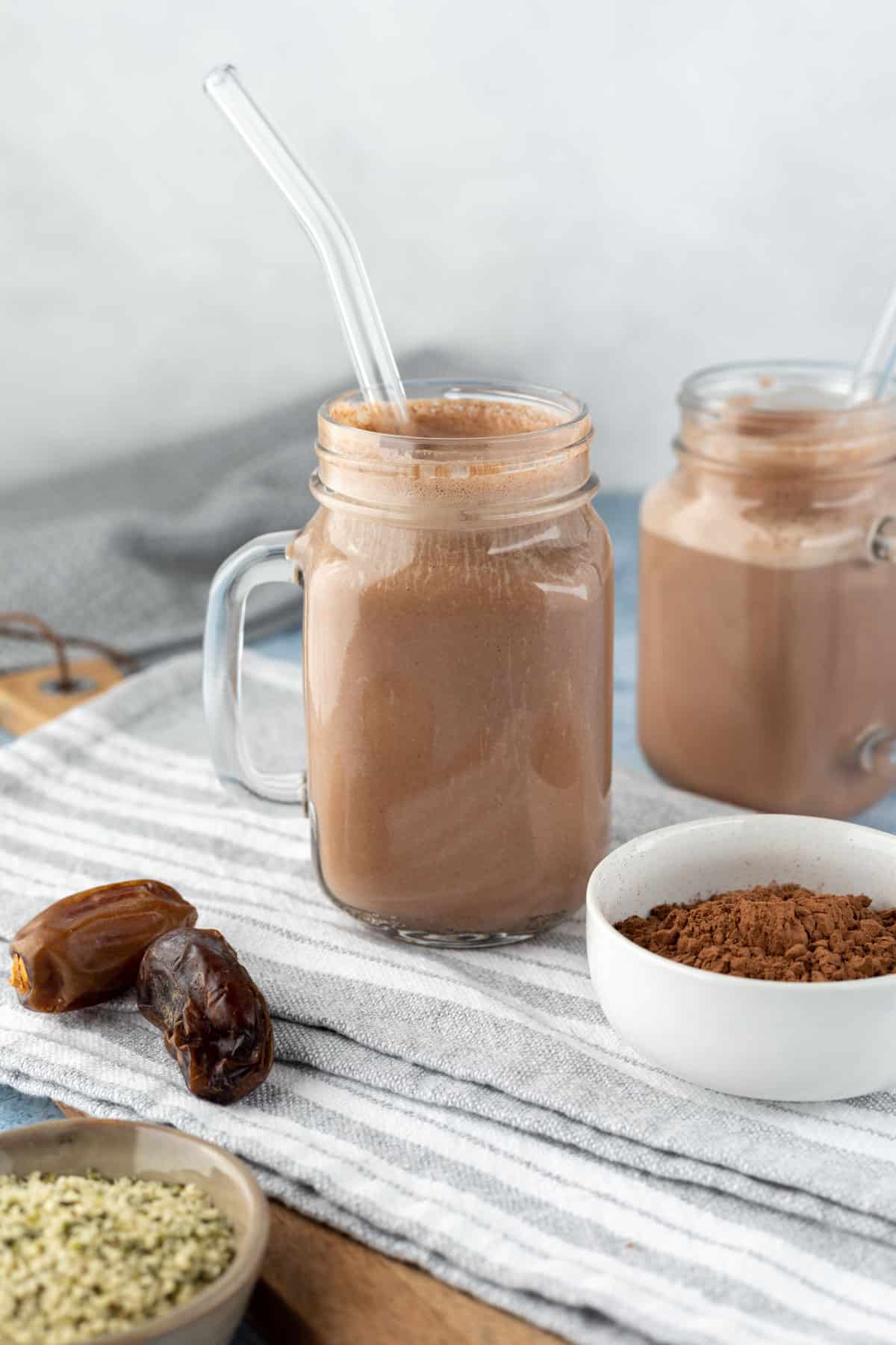 two glass jars filled with chocolate hemp milk against a gray background.