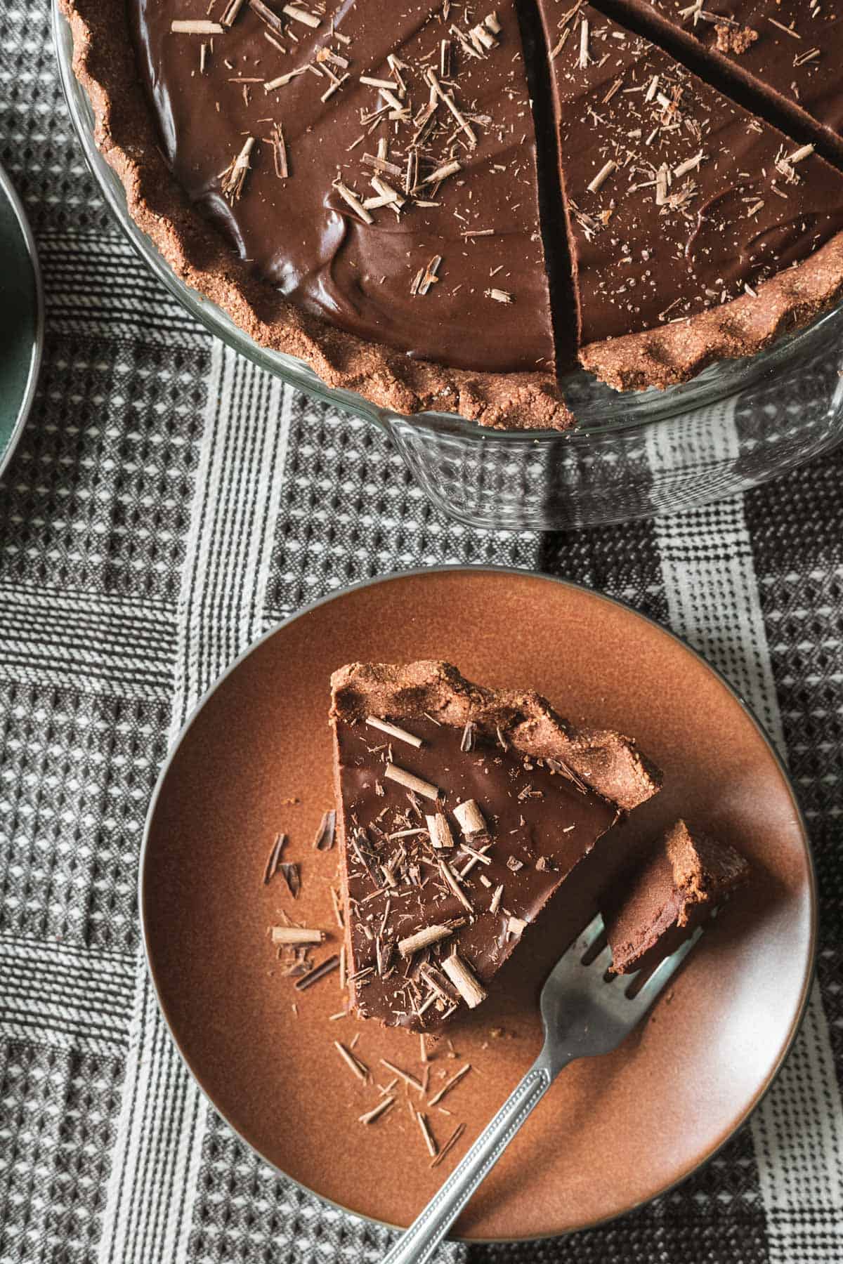 rich and dark chocolate pie on a rust colored plate with the whole pie in background.