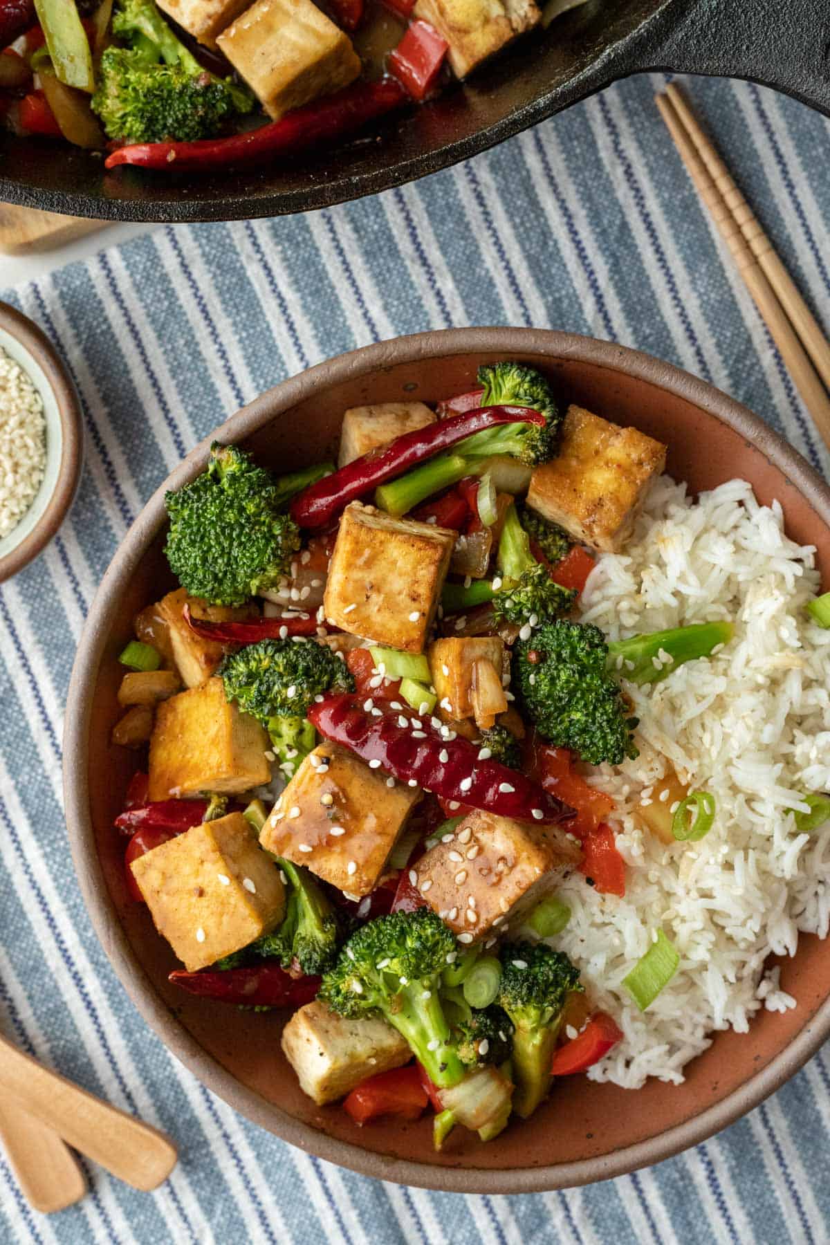 overhead view of a colorful bowl of Szechuan tofu, veggies and rice in a red bowl.