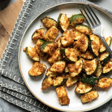 golden air fried zucchini with panko breading on a white plate.