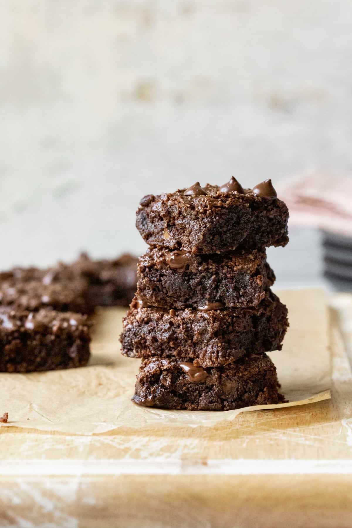 Four gooey and moist almond flour brownies stacked on a wood cutting board.