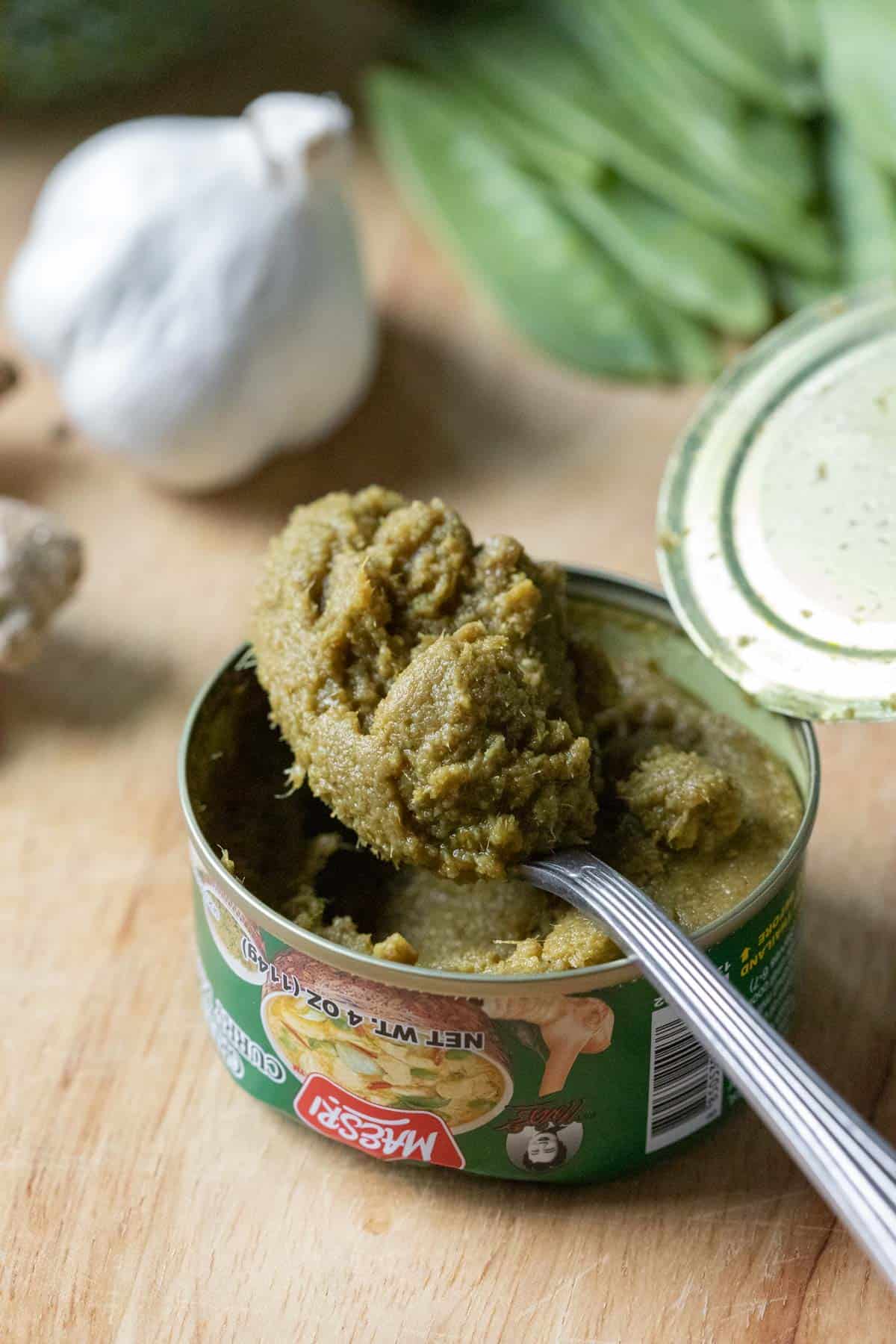 a spoon scooping up Maesri brand Thai green curry paste from a can.