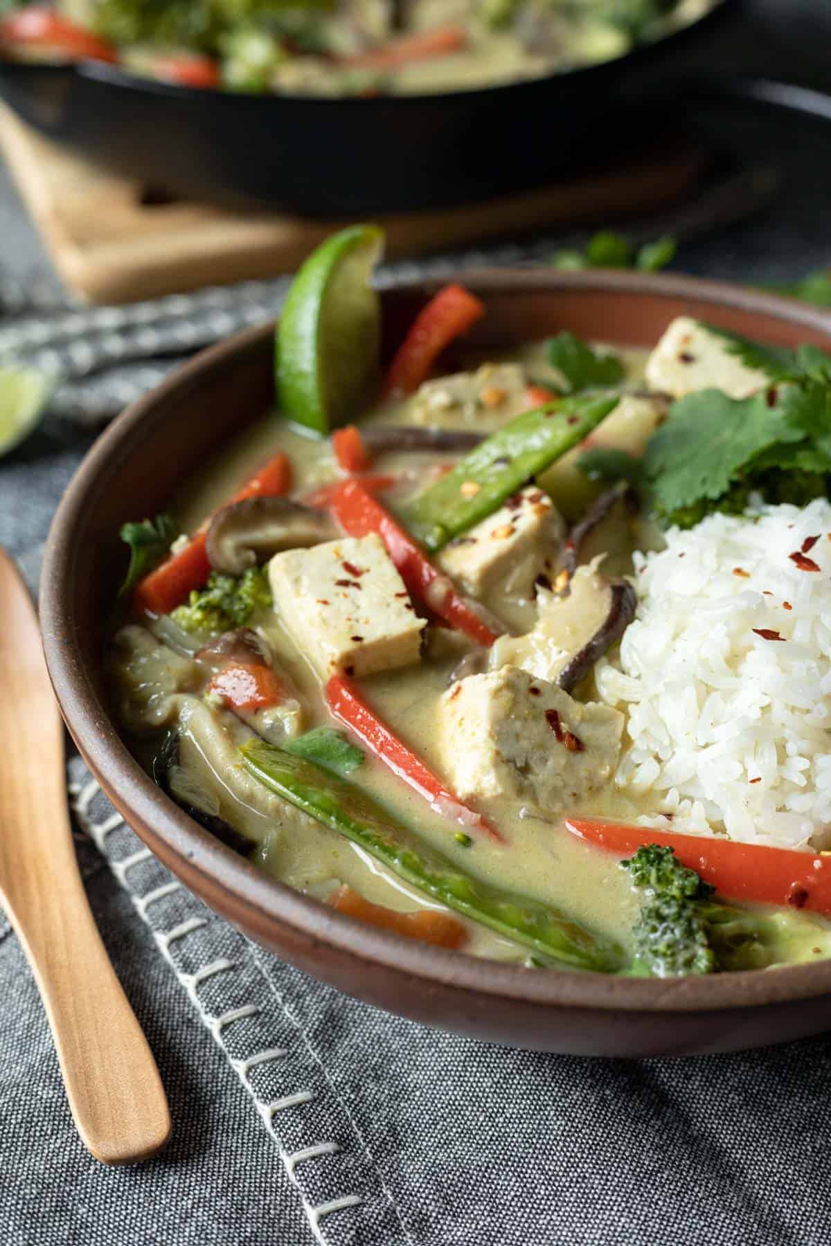 a serving of tofu curry with a scoop or rice in a red bowl.