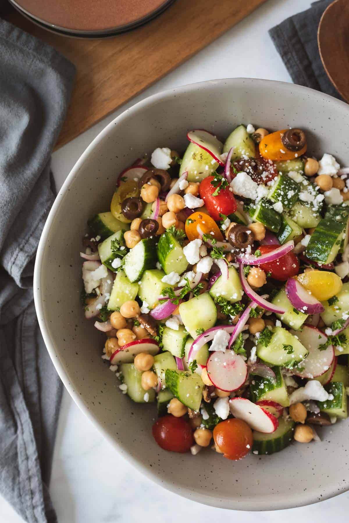 large gray serving bowl filled with colorful cucumber salad sprinkled with feta.