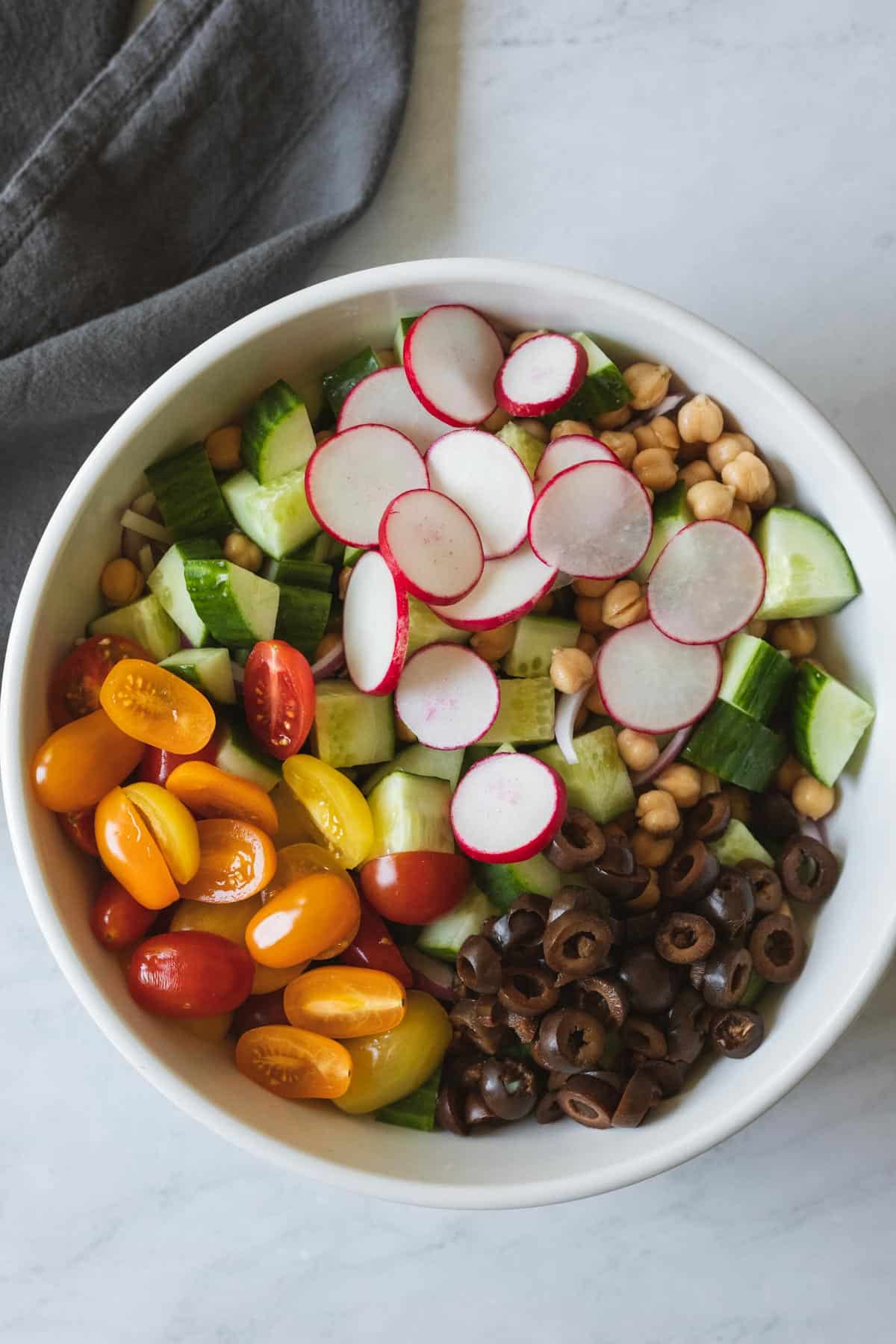 assembling all ingredients for Mediterranean cucumber salad in a large bowl.