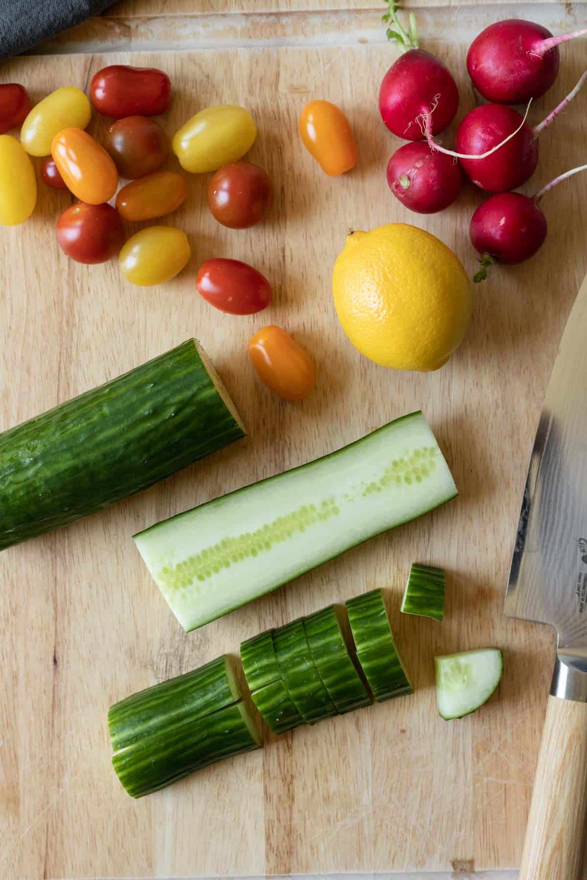 Chopping cucumber and other veggies on a large cutting board.