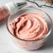 a cupcake topped with swirls of vegan strawberry frosting and half of a fresh strawberry.