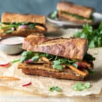 Banh mi sandwiches on a cutting board, dressed with cilantro and pickled vegetables.