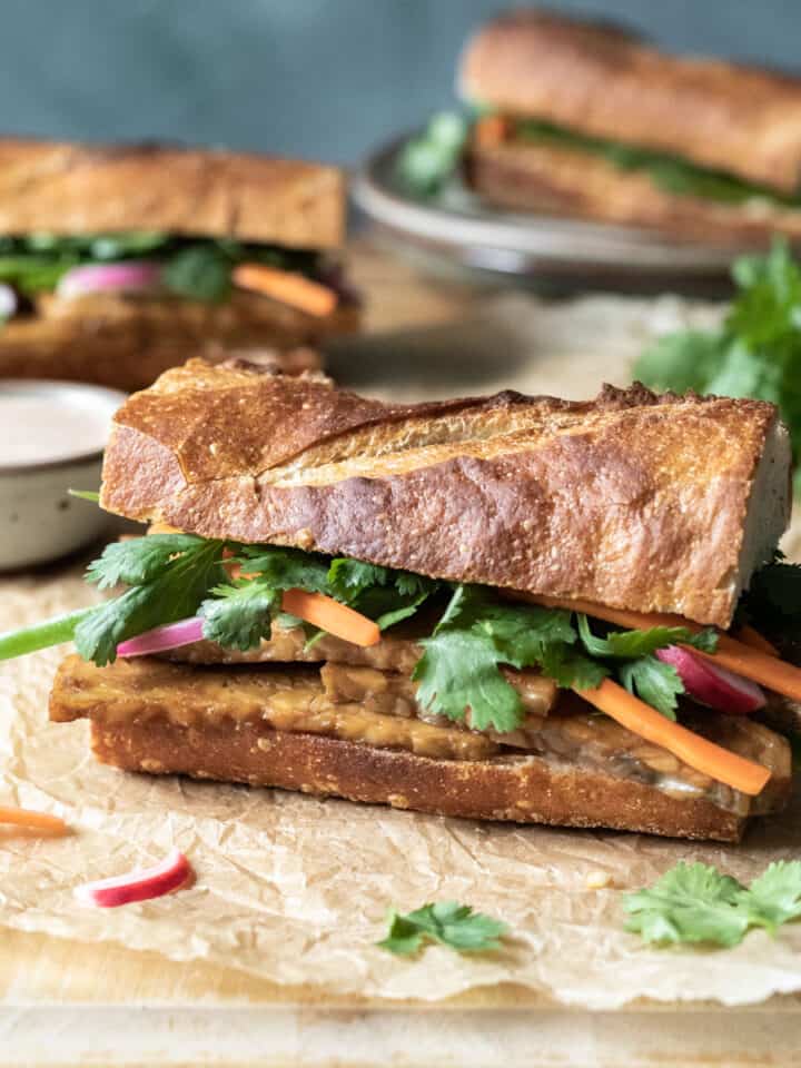 Banh mi sandwiches on a cutting board, dressed with cilantro and pickled vegetables.