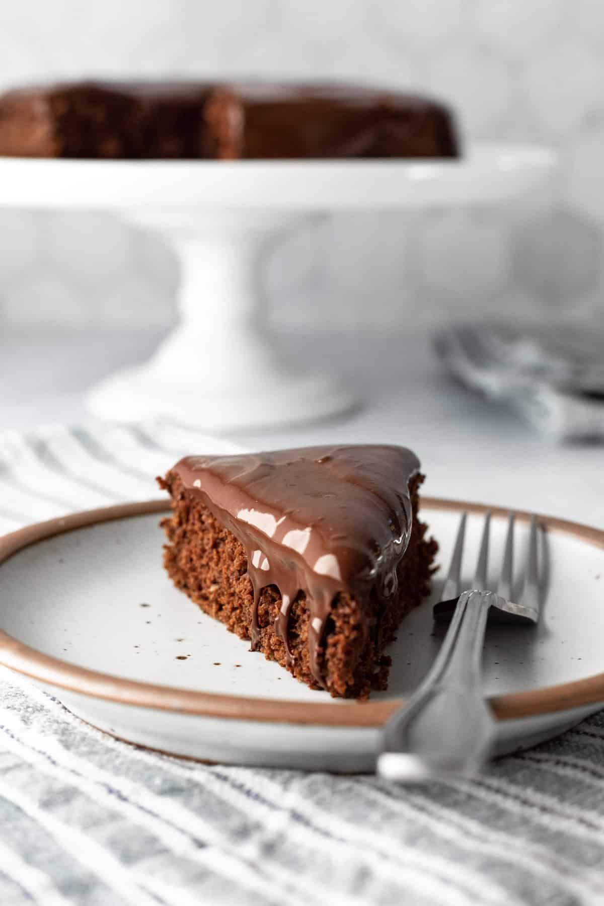 a slice of cake topped with shiny, spreadable, vegan ganache on a small plate.